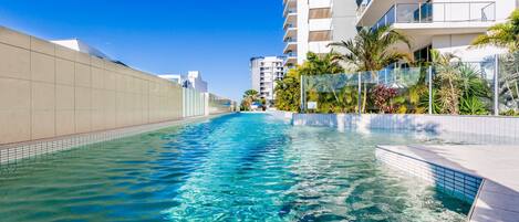 A swimming pool with clear water, surrounded by modern buildings and palm trees.