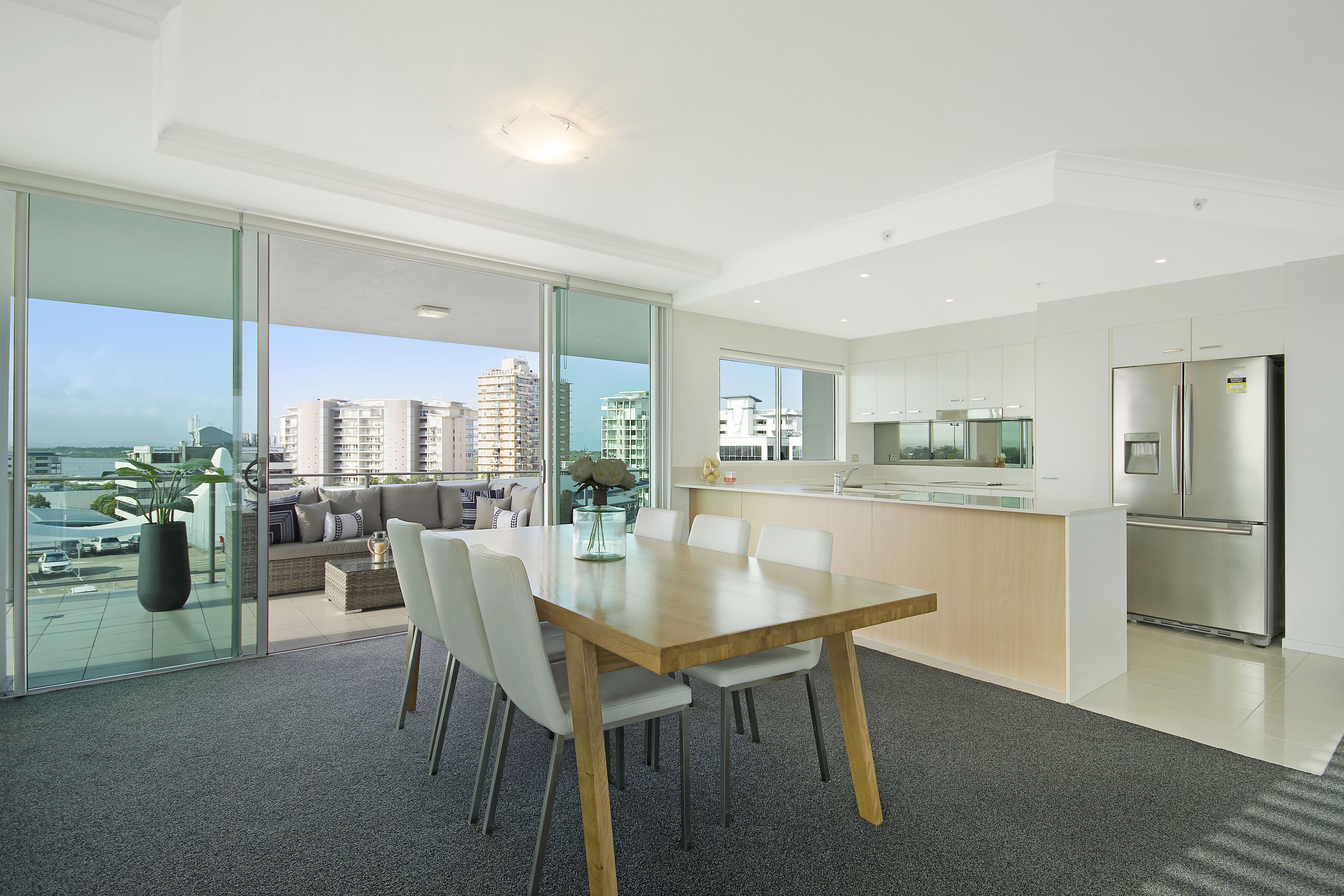 A modern apartment with a dining area, kitchen, and a balcony with a city view.