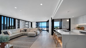 Una sala de estar moderna con un amplio sofá modular, un comedor y una cocina con encimera de mármol.