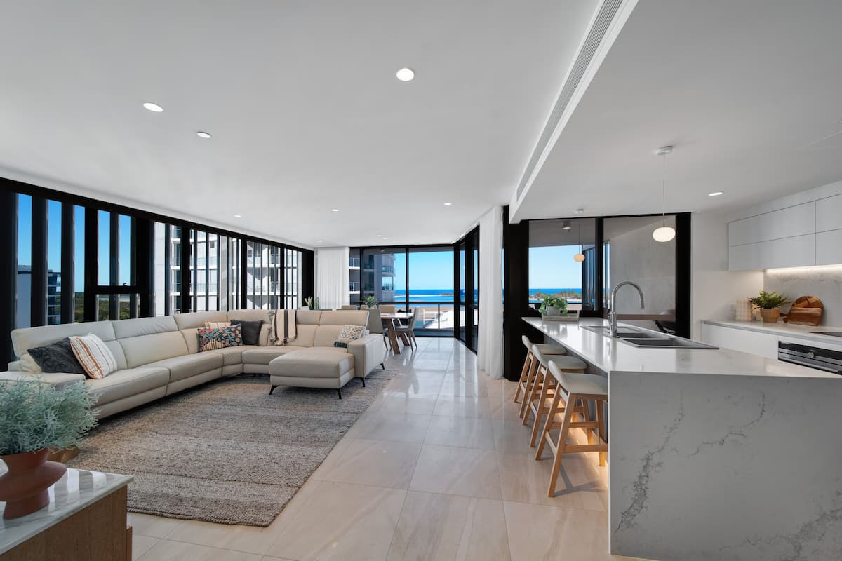 A modern living room with a large sectional sofa, a dining area, and a kitchen with a marble countertop.