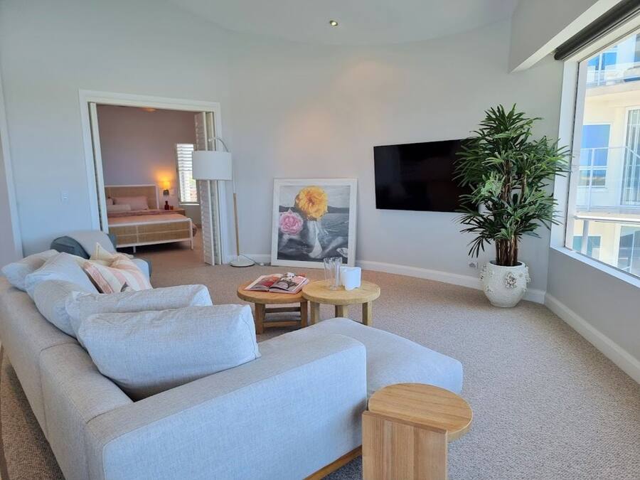 A modern living room with a grey sofa, a small wooden table, a potted plant, and a framed artwork.