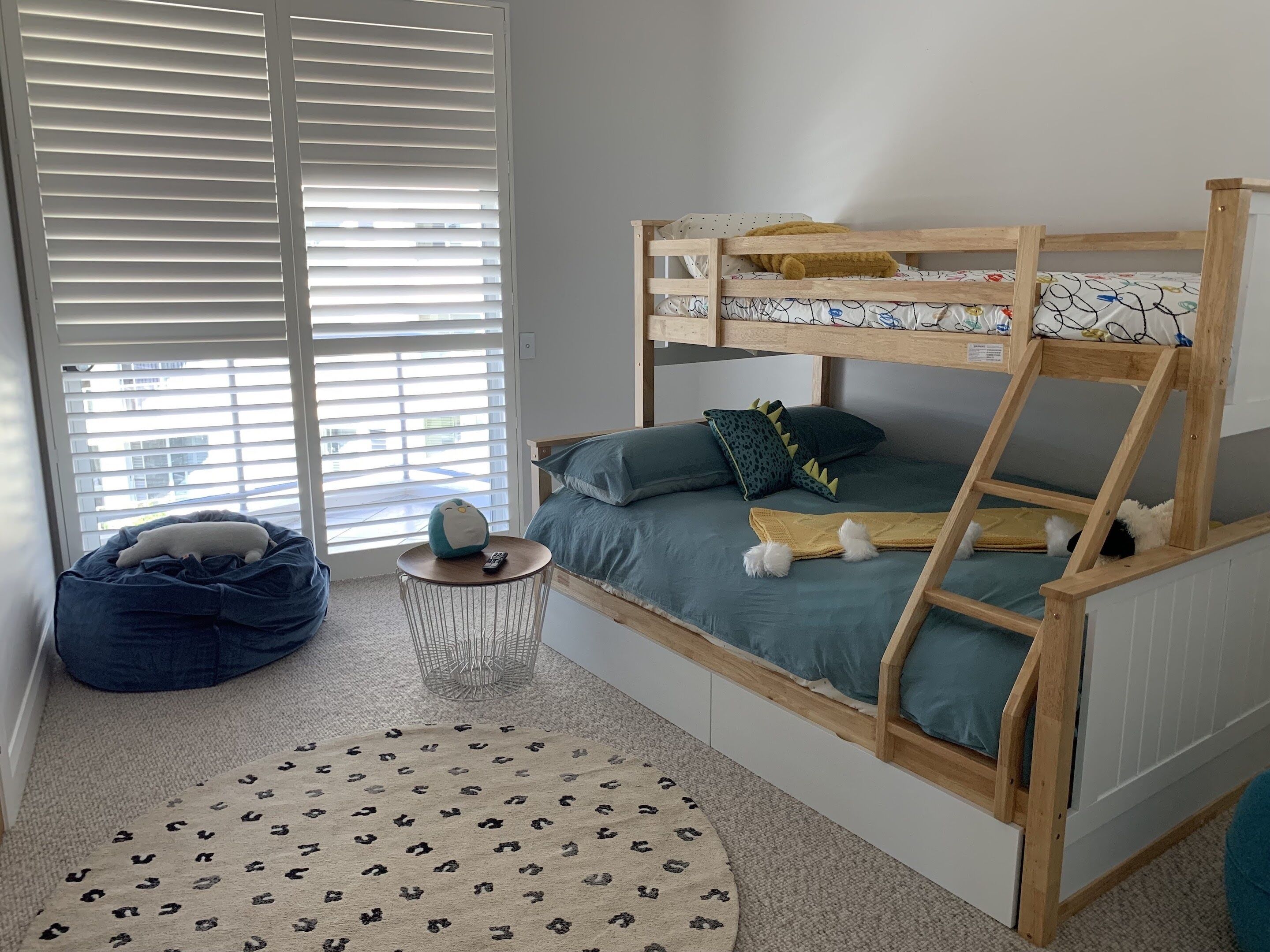 A bunk bed with a ladder, a bean bag chair, a small round table with a remote control, and a leopard print rug.