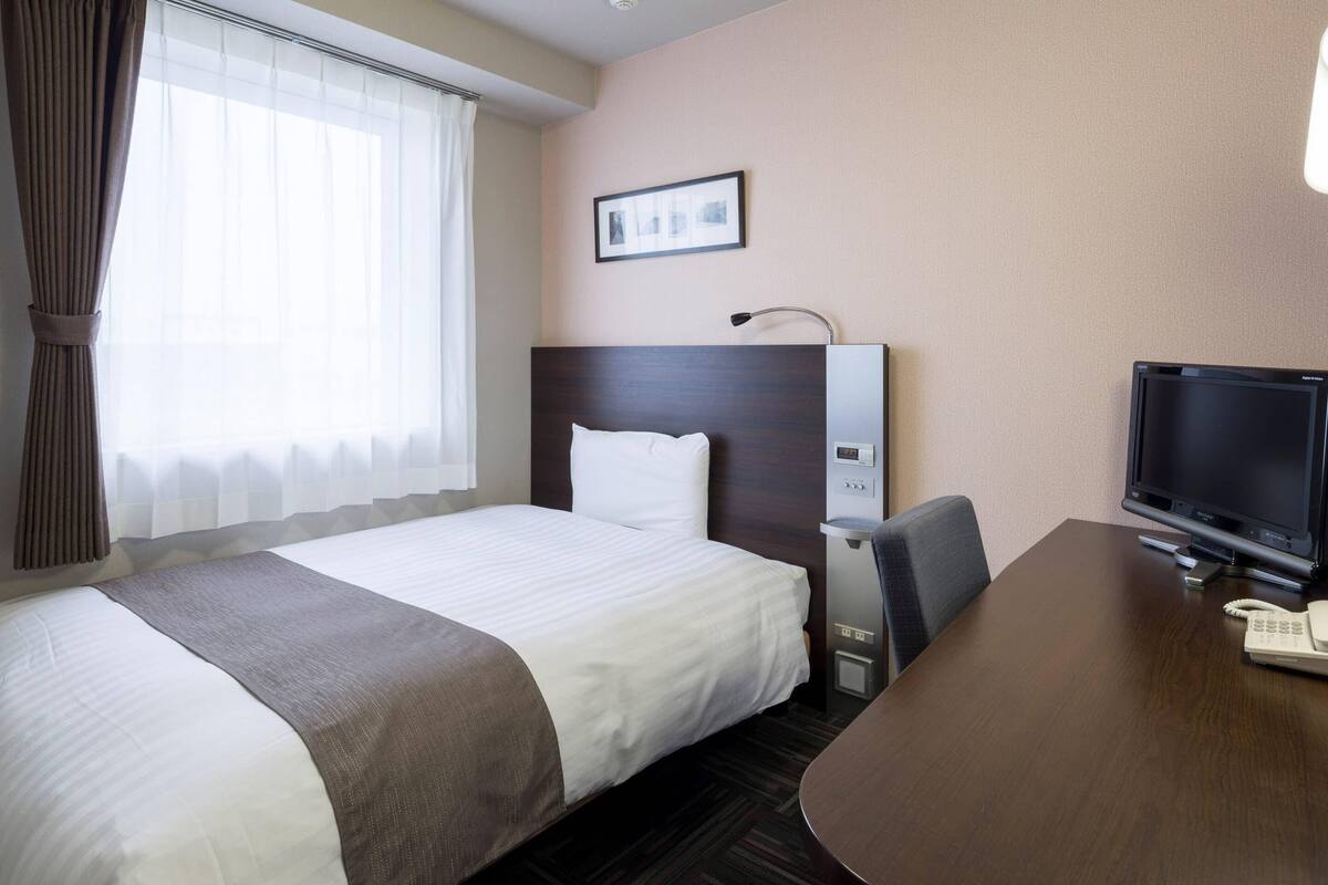 A hotel room with a bed, a desk, a television, and a picture on the wall.