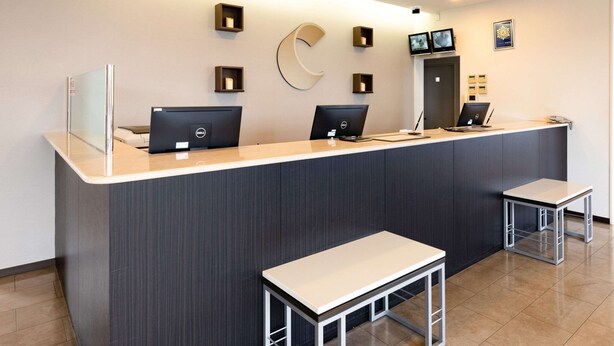 A reception desk with two computers, a large C-shaped wall decoration, and two small tables.