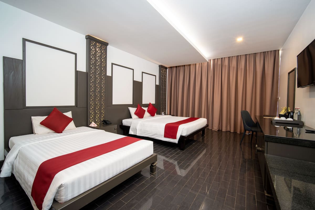 A hotel room with two beds, a desk, a chair, and a television.
