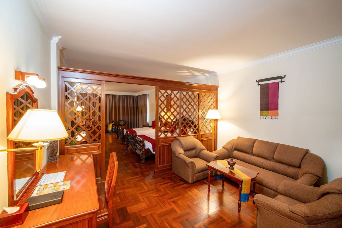 A hotel room with a wooden floor, a sofa, a dining table with chairs, and a decorative partition.