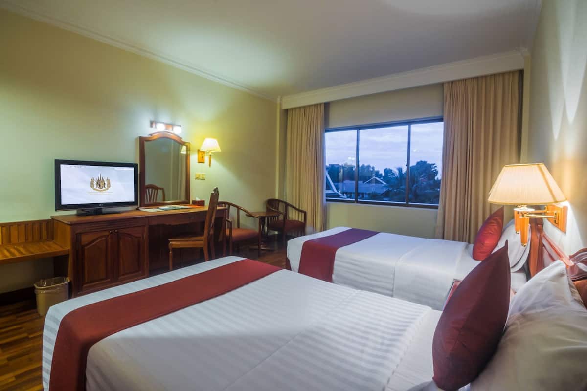 A hotel room with two beds, a desk, a television, and a window with a view.