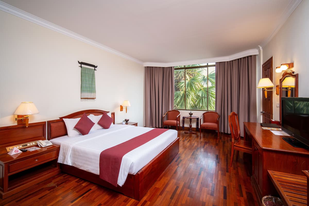 A hotel room with a large bed, wooden furniture, a desk with a television, and a window with curtains.