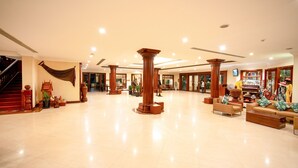 A spacious lobby with high ceilings, large wooden columns, a grand staircase, and a seating area with sofas and a coffee table. - Khemara Angkor Hotel & Spa (Siem Reap)