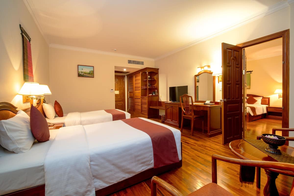 A hotel room with two beds, a desk, a chair, a dining table, and a wardrobe.