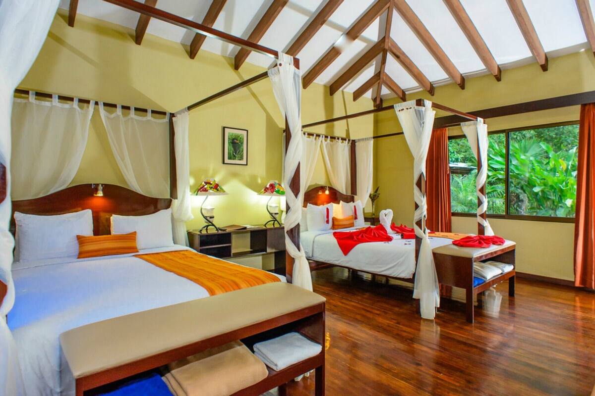 A room with two beds, each with a canopy, wooden headboards, and a bedside table with a lamp.