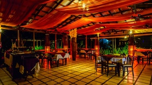 An indoor dining area with tables and chairs, a tiled floor, and a ceiling with draped fabric.