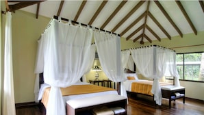 A room with two beds, each with a canopy. The room has wooden flooring and a sloped ceiling with wooden beams.