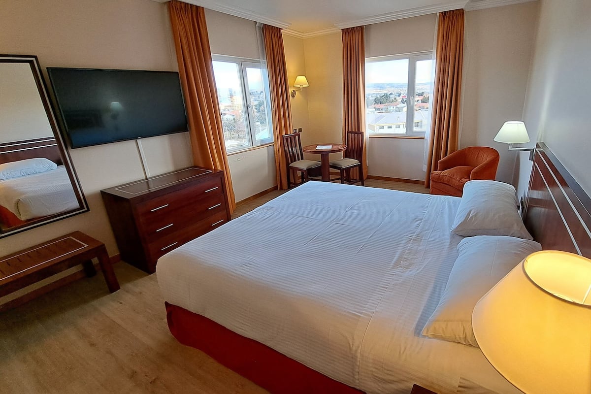 A hotel room with a large bed, a desk, a chair, a lamp, and a TV.