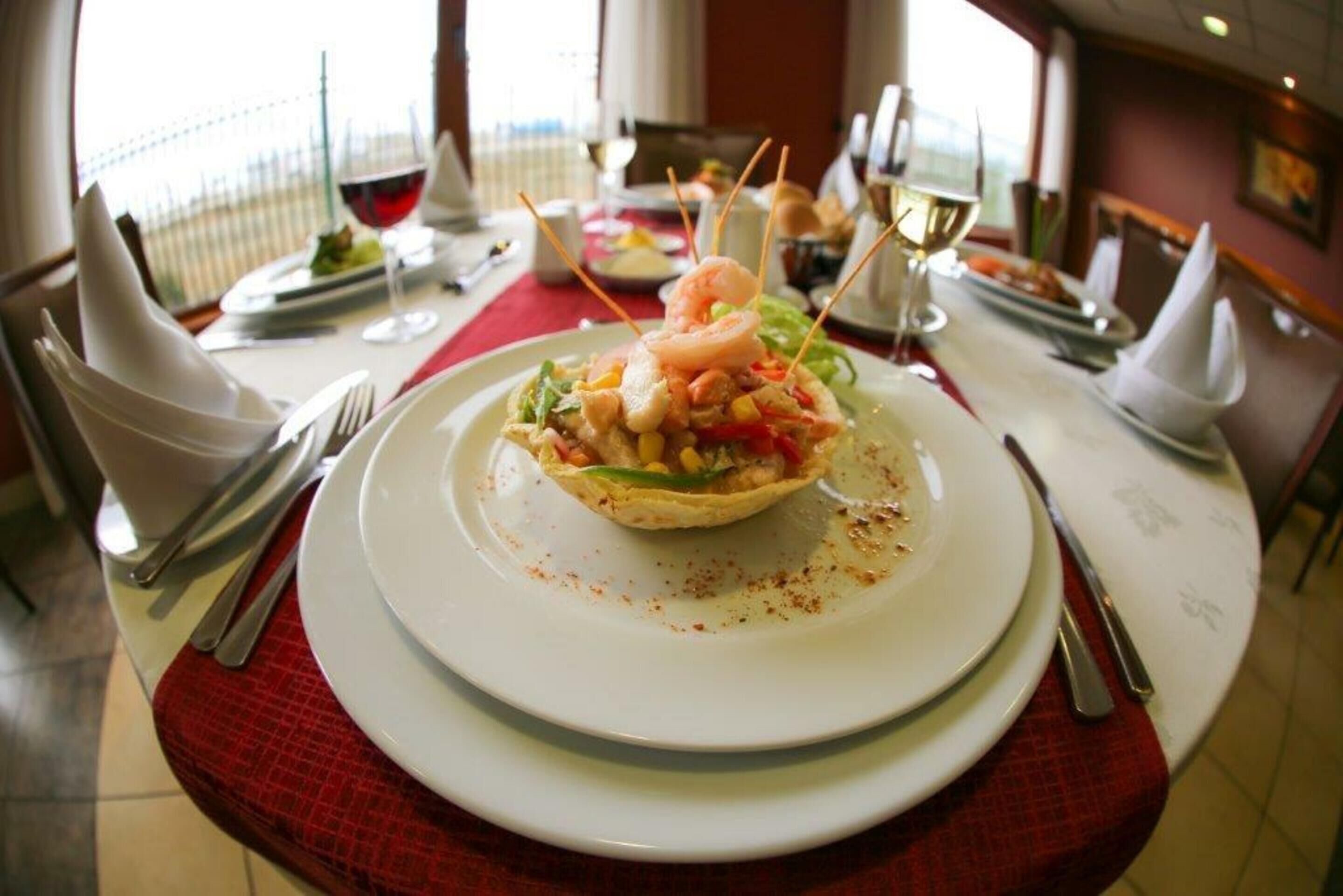 Un tavolo da pranzo con un piatto di pesce, bicchieri da vino e una tovaglia rossa.