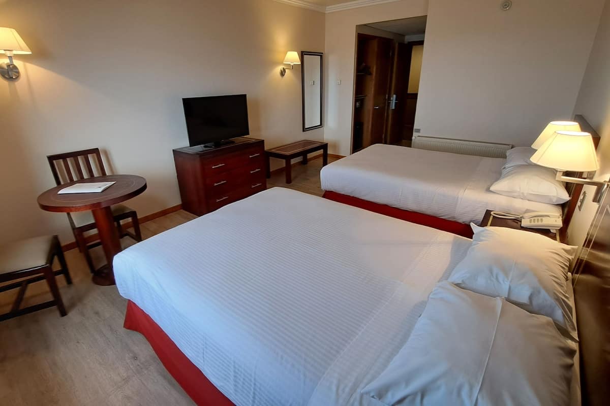A hotel room with two beds, a desk, a chair, a television, and a lamp.