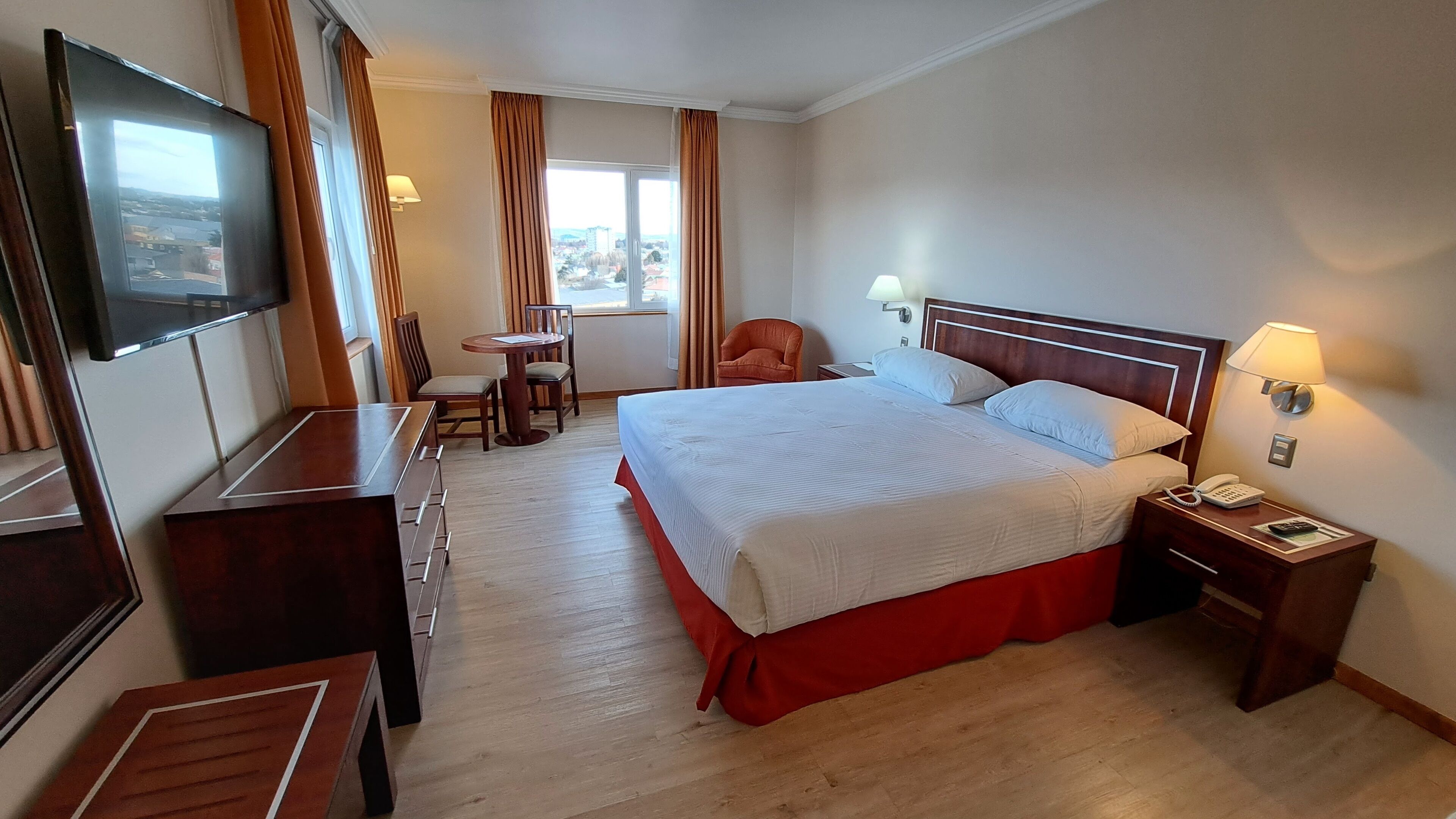 A hotel room with a large bed, a desk with a chair, a TV, and a window with curtains.