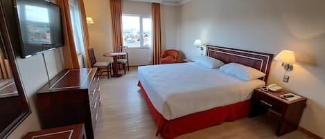 A hotel room with a large bed, a desk with a chair, a TV, and a window with curtains.