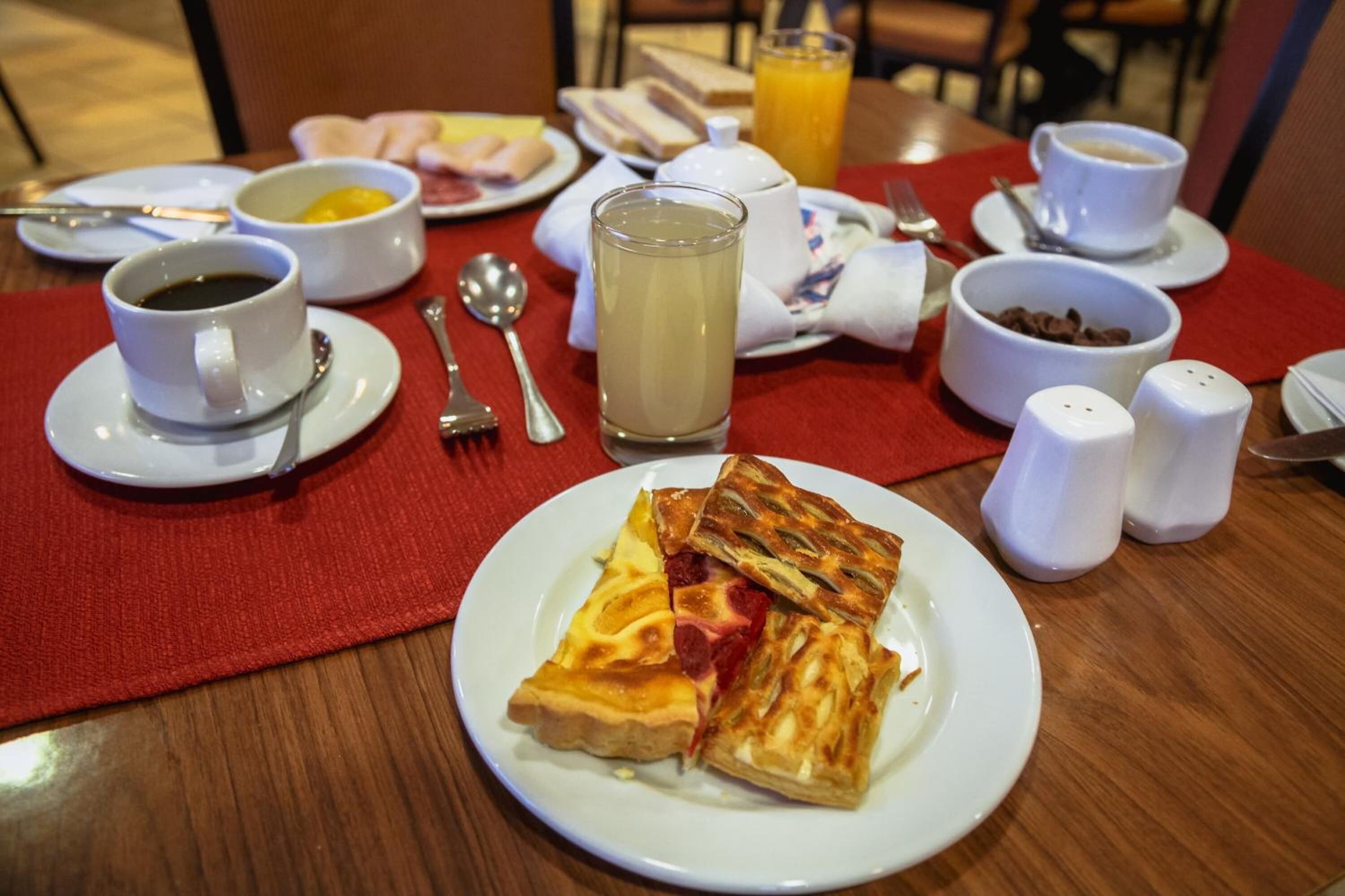 Ein Frühstückstisch mit Gebäck, einem Glas Saft, Kaffeetassen und einer Schüssel Müsli.