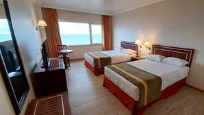 A hotel room with two beds, a desk with a TV, a small table, and a window with a view of the sea. - Diego De Almagro Punta Arenas (Punta Arenas)