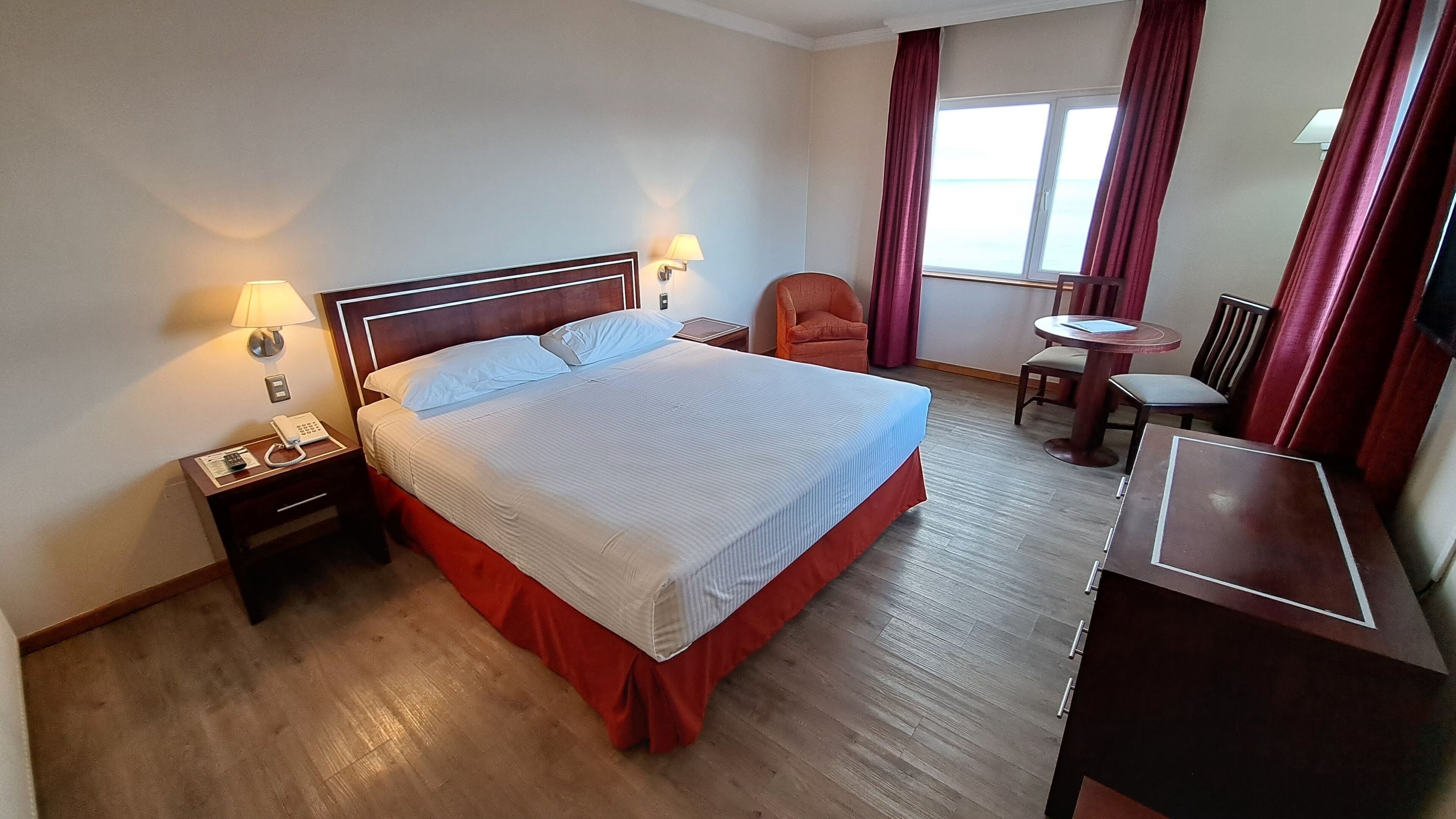 Una habitación de hotel con una cama, lámparas de noche, un escritorio y una silla.