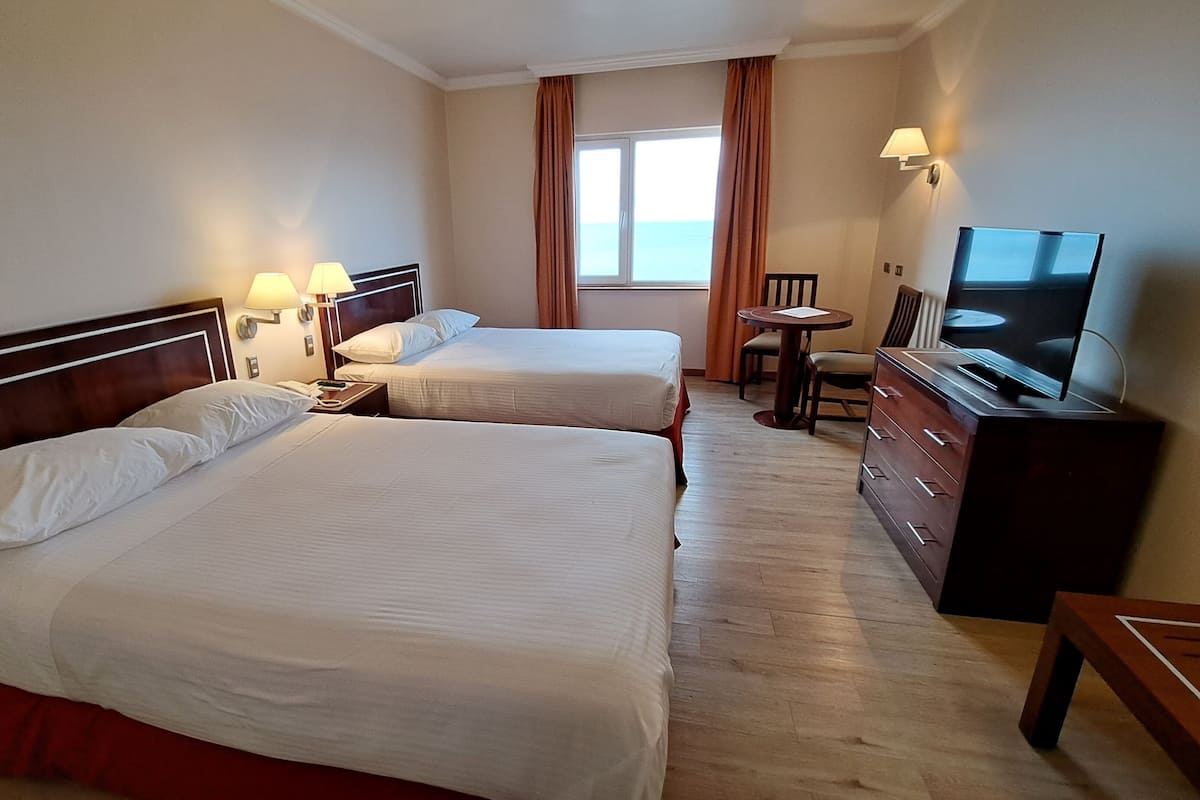 A hotel room with two beds, a TV, a desk, and a window with curtains.