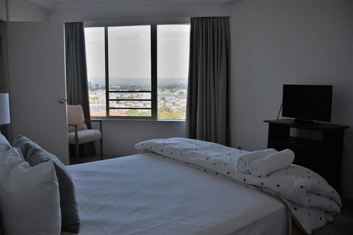 A hotel room with a bed, a chair, a desk with a TV, and a window with curtains.