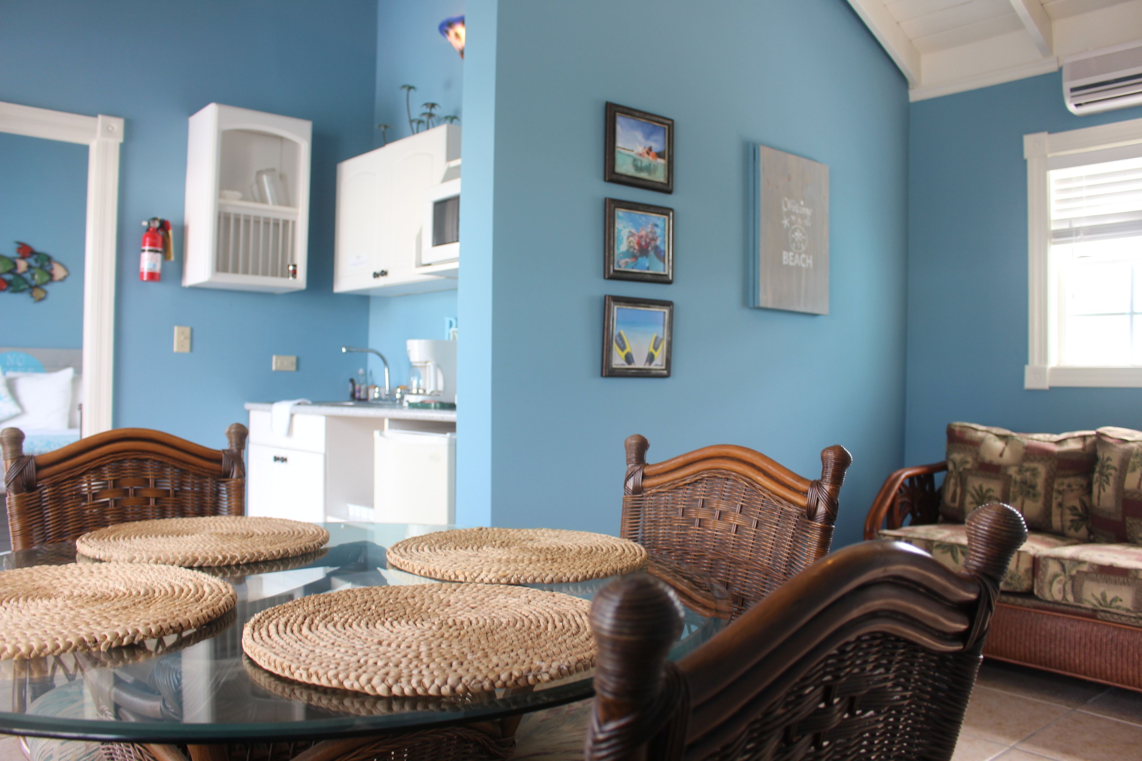 A dining area with a glass table, wicker chairs, and a sofa.