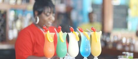 A bar with a bartender in a red shirt and a selection of colorful drinks on the counter.