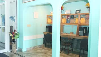 Ein Empfangsbereich mit hellblauer Wand, Fliesenboden, einer Rezeption mit Computer und einer Pflanze.