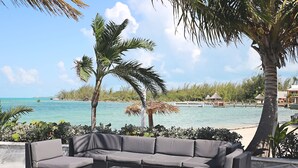 A seaside patio with a sectional sofa and a coffee table, overlooking a beach and turquoise waters. - Hideaways Exuma (George Town)