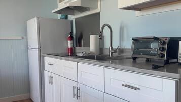 A modern kitchen with white cabinets, a stainless steel refrigerator, a built-in oven, a microwave, and a toaster.