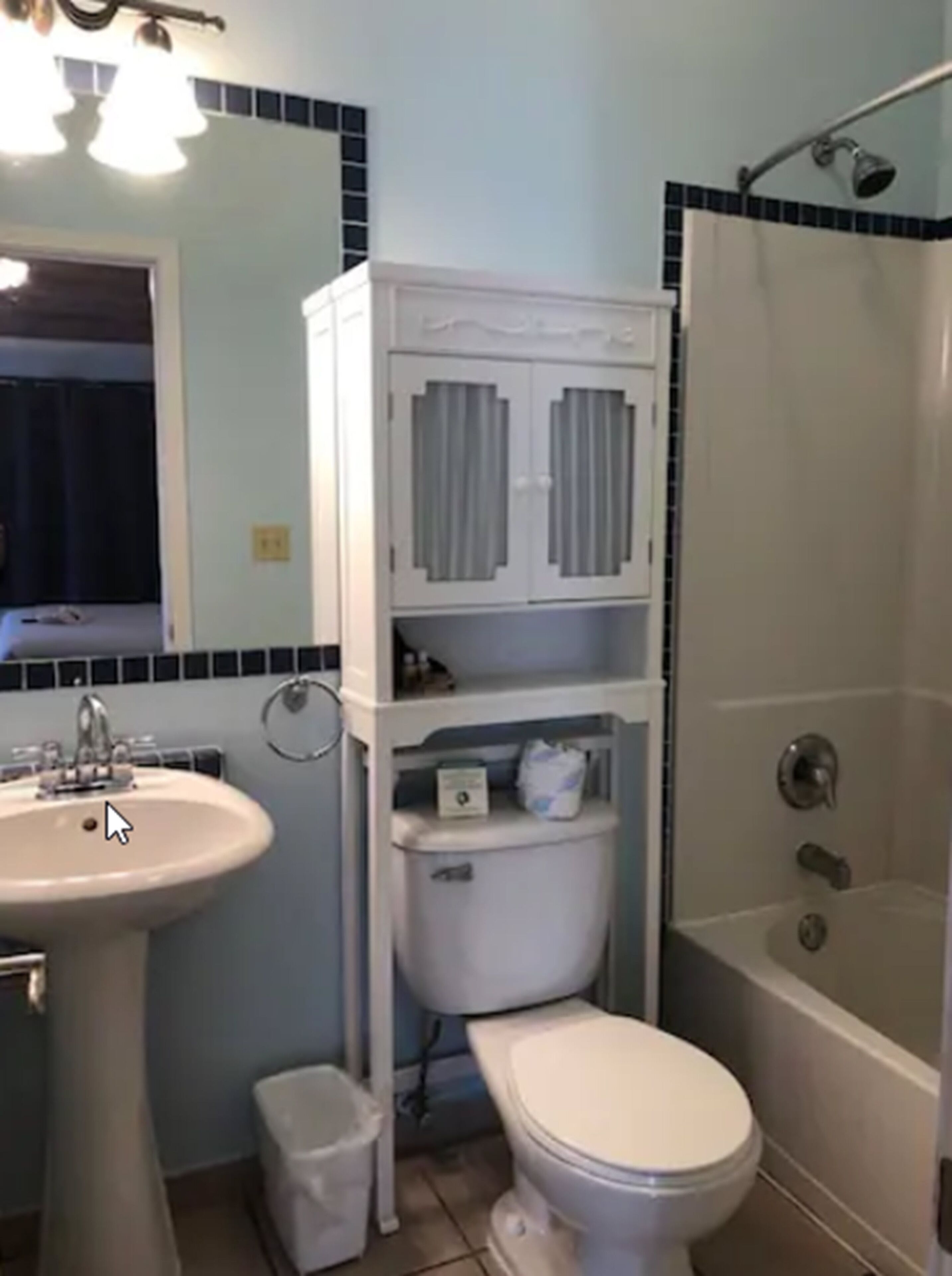 A bathroom with a sink, toilet, and bathtub. There is a cabinet above the toilet and a small trash bin next to it.