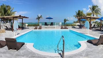 Una piscina al aire libre, sombrillas, sillones reclinables de piscina