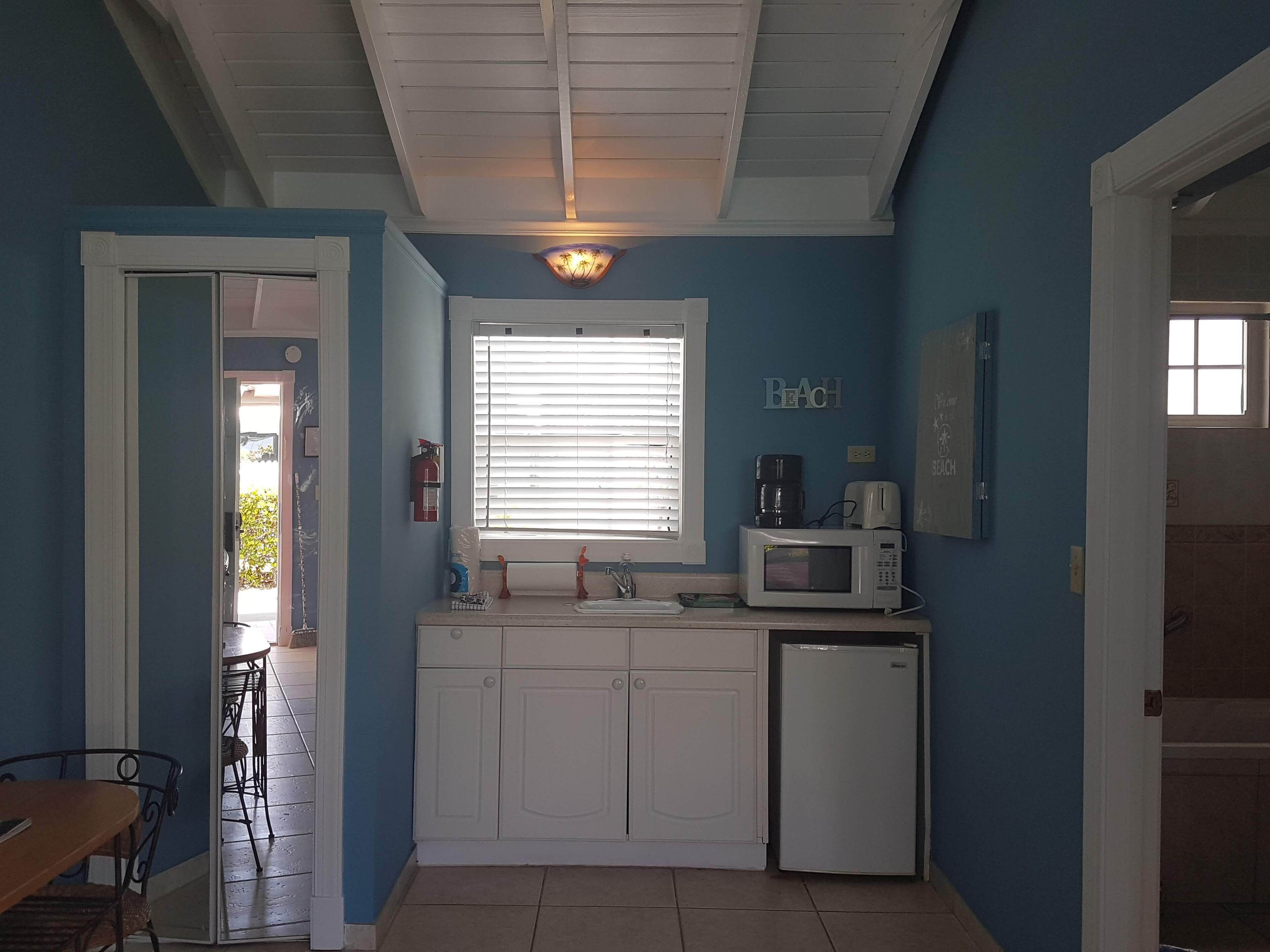 A compact kitchen with white cabinets, a microwave, a coffee maker, and a sink.