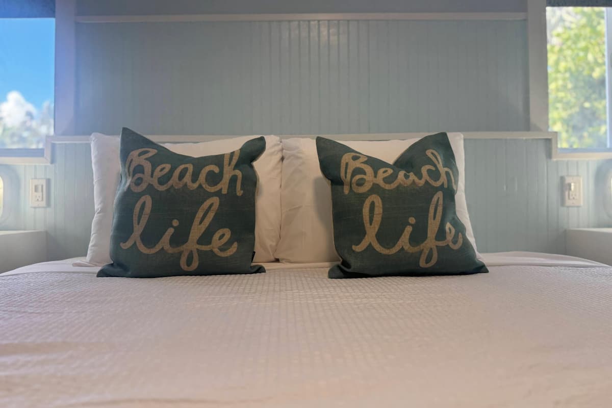 Una cama con dos almohadas que dicen "Beach life" y un cabecero blanco.