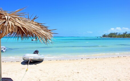 A beach with a boat tied to a palm tree, clear blue water, and a distant island.