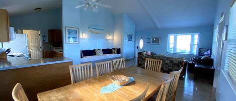 A spacious living area with a wooden dining table, chairs, a sofa, and a ceiling fan.