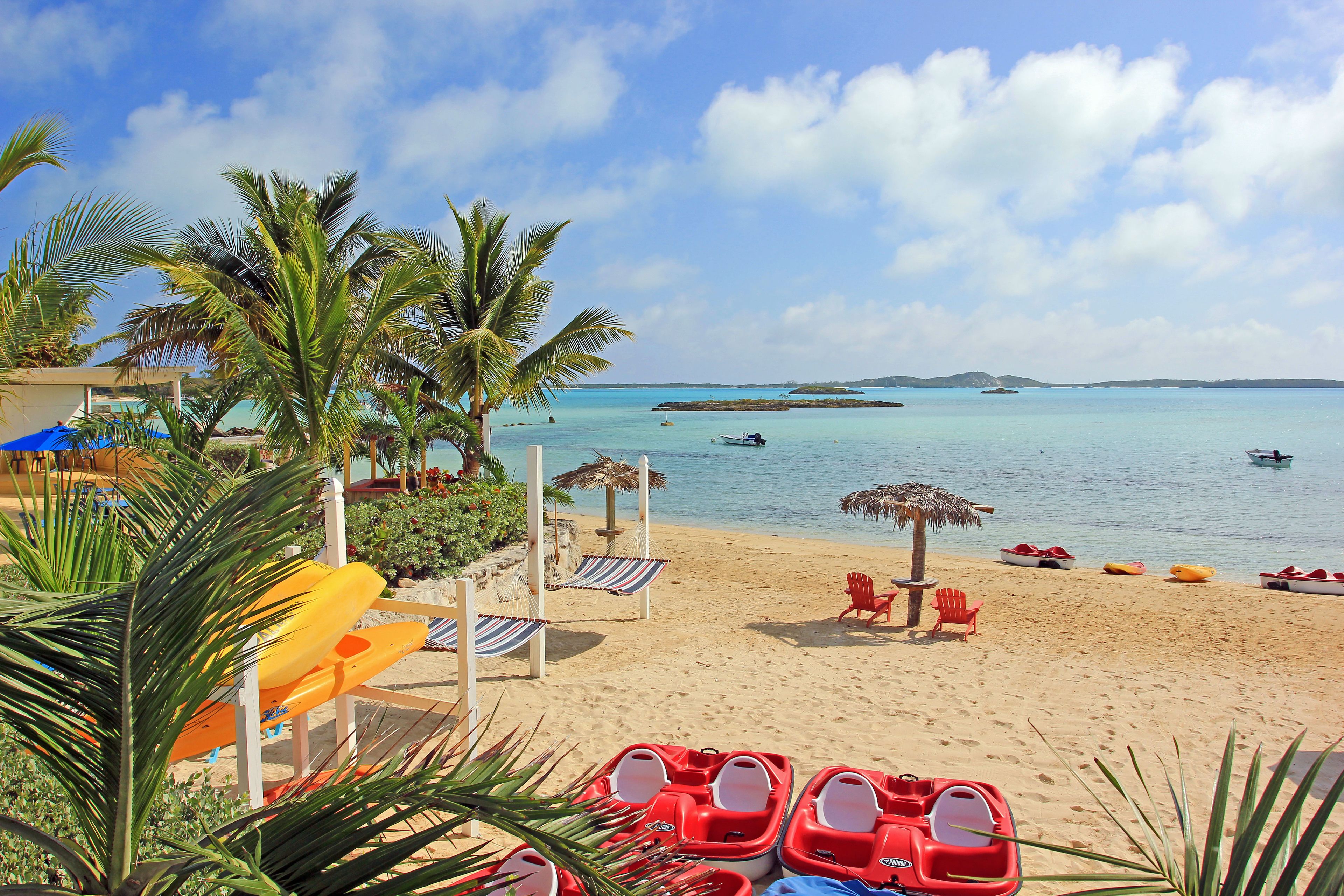 A beach with red lounge chairs, a thatched umbrella, and a water slide.