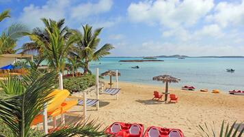 A beach with red lounge chairs, a thatched umbrella, and a water slide.
