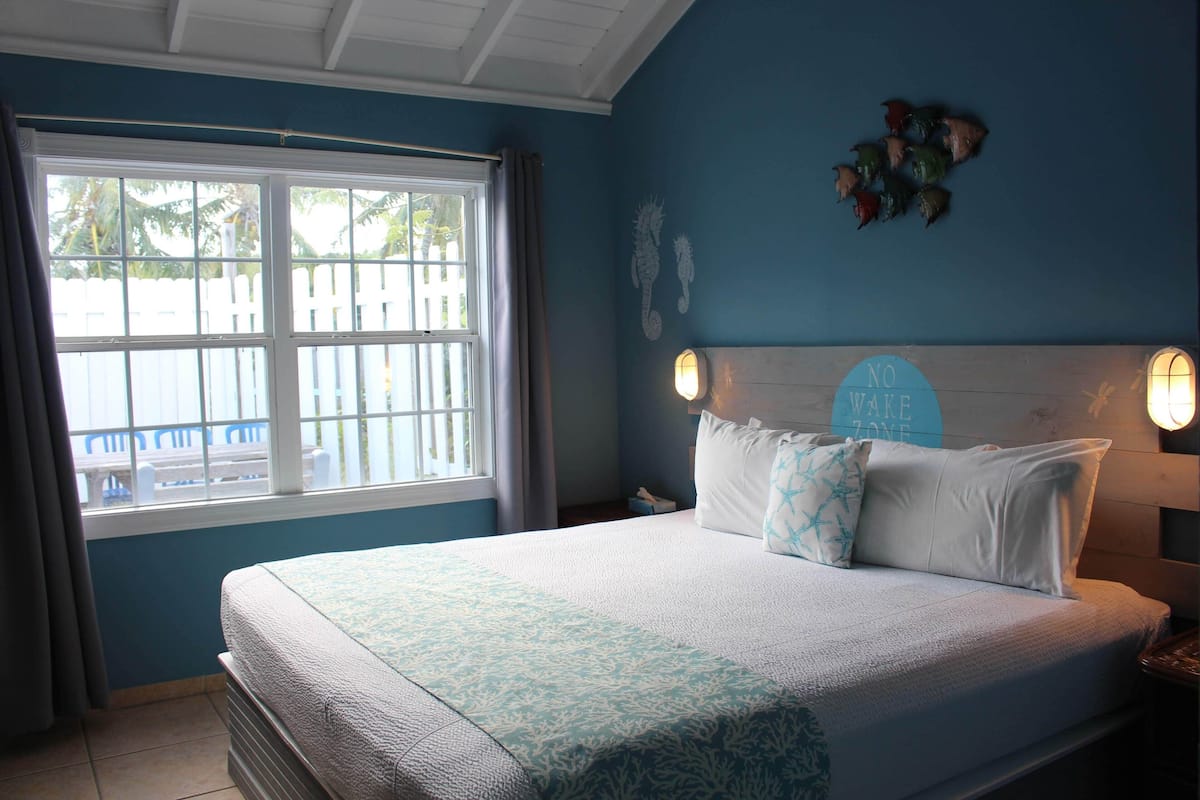 Un dormitorio con una cama, una ventana con cortinas, un reloj de pared y un adorno en la pared.