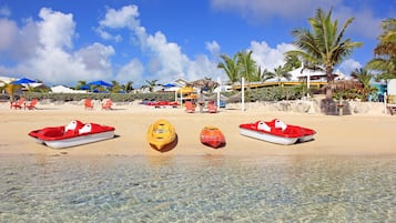 Una playa con agua clara y poco profunda, varias kayaks y sombrillas.