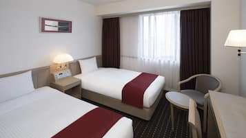 Une chambre d’hôtel avec deux lits, un bureau, une chaise, une lampe et une fenêtre avec des rideaux.