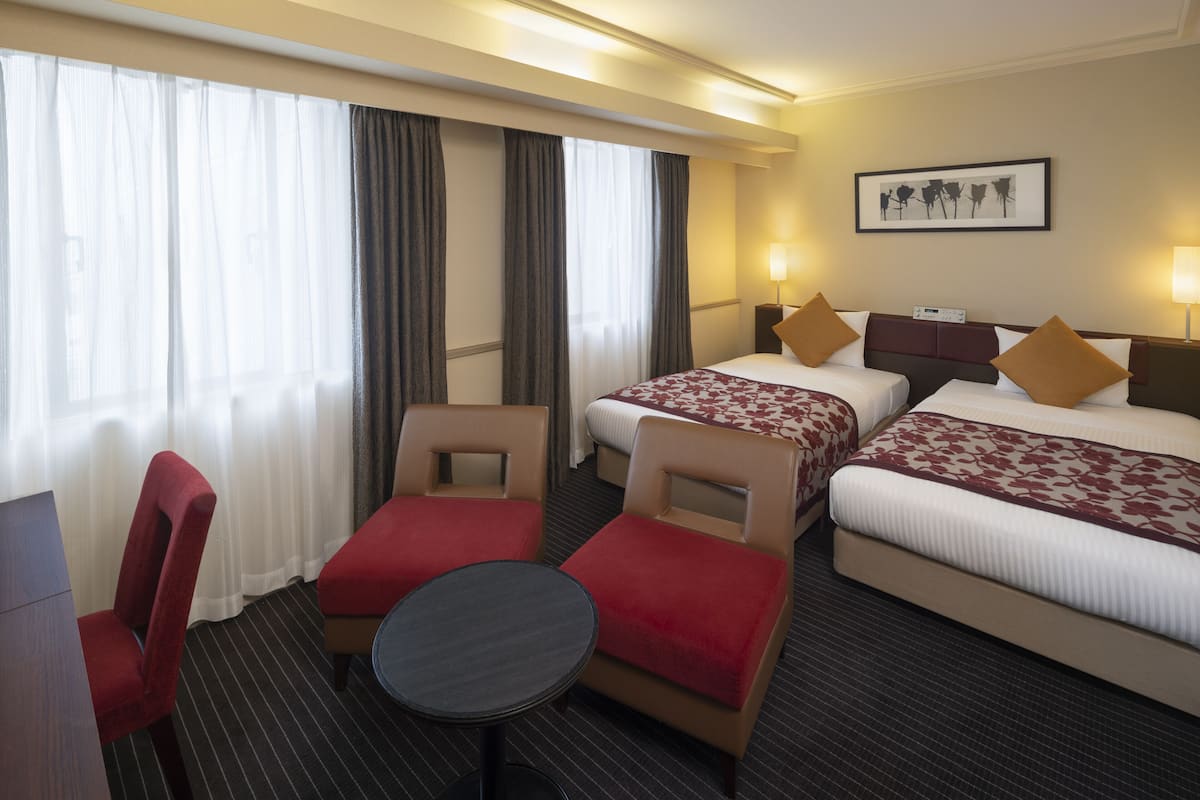 A hotel room with two beds, a desk, a chair, and a small table.