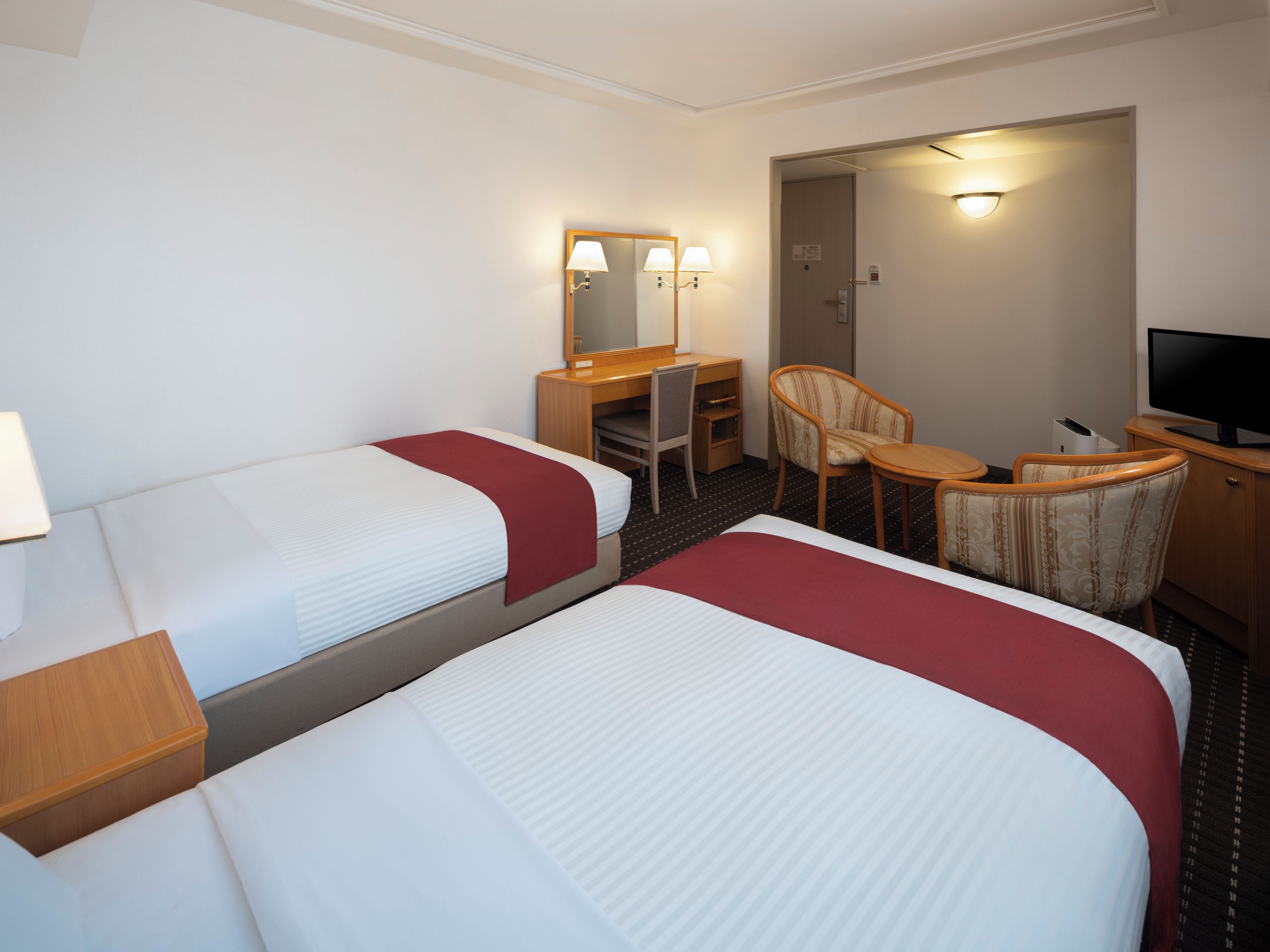 A hotel room with two beds, a desk, a chair, a television, and a mirror.