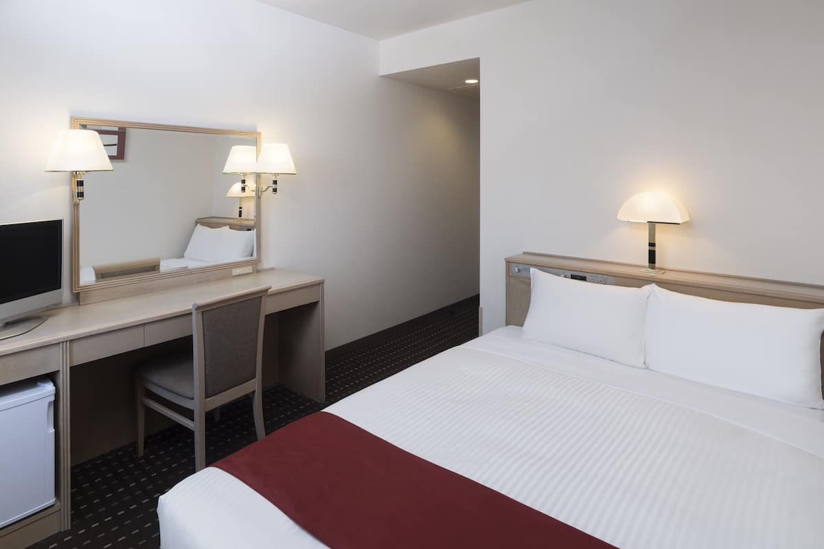 A hotel room with a bed, a desk, a chair, a television, and two lamps.