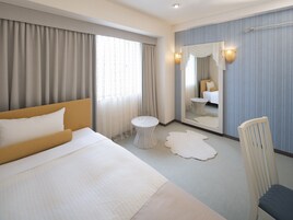 Quarto de hotel com uma cama grande, uma mesa de apoio redonda, uma cadeira, um espelho e vista para outro quarto.