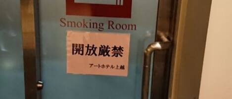 A door with a smoking room sign and a no-smoking notice in another language.