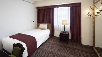 A hotel room with a bed, a nightstand with a lamp, a chair, and a large mirror.