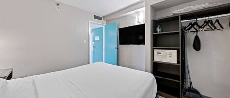 A hotel room with a bed, a wardrobe with a TV, and a security system.